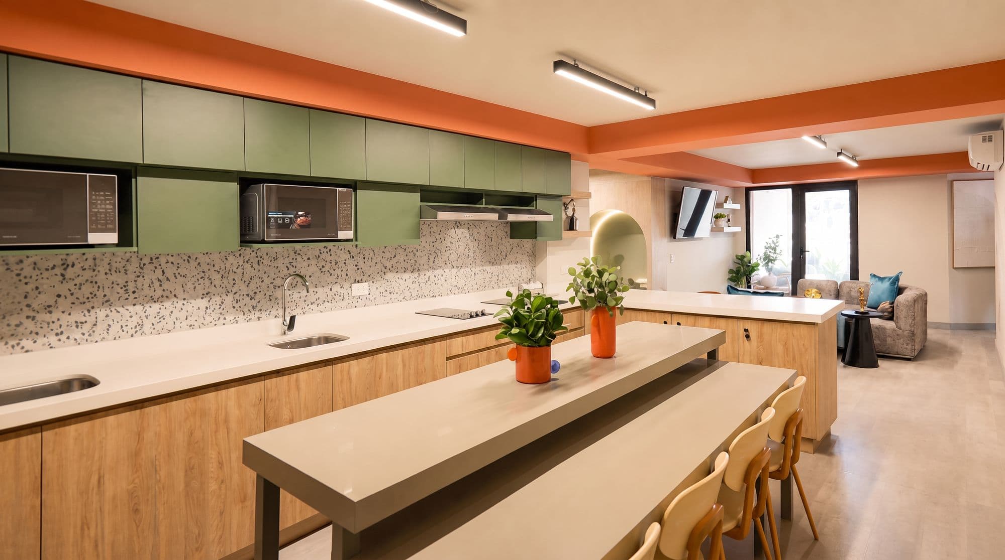 Cocina comunal verde con isla larga y respaldo de terrazo