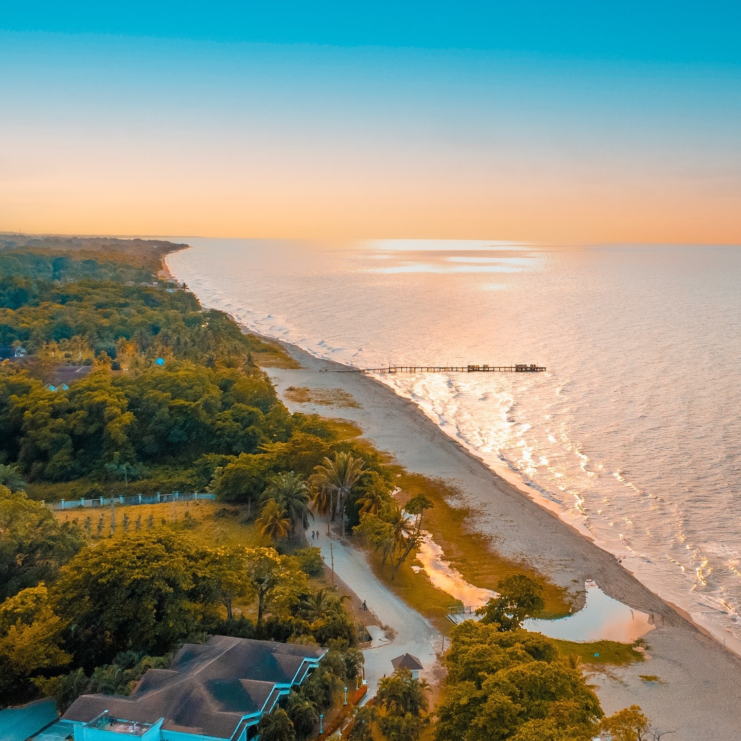 Vista aérea de la costa al atardecer, con la playa curvándose hacia el horizonte