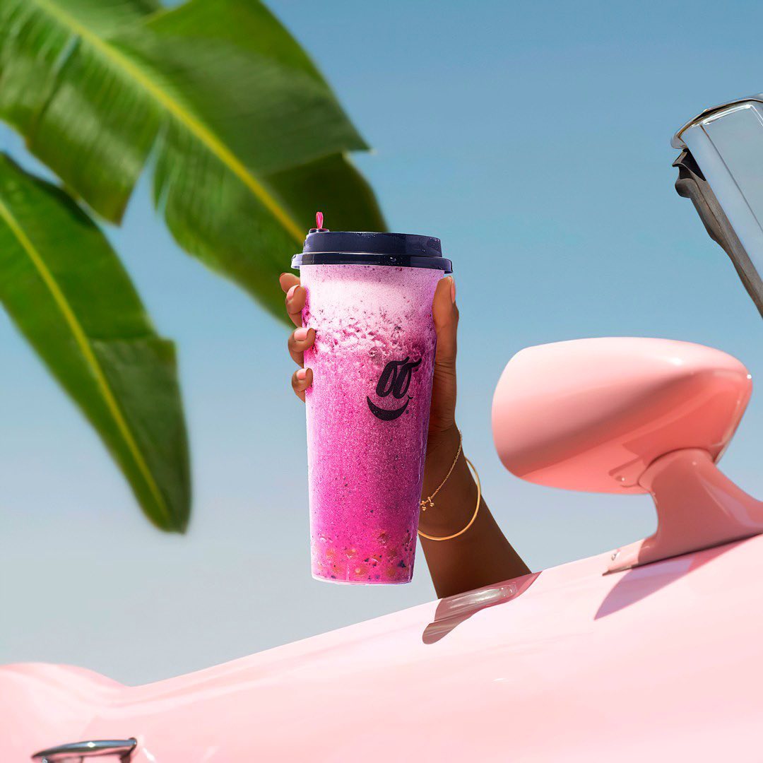 Bubble tea rosado en la mano, apoyado en un carro rosado